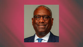 Executive headshot of James Sills in a blue suit and patterned tie with glasses and a neutral backdrop.