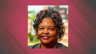 Professional headshot of Kim Ratliff smiling in a gray blazer with curled hair and subtle red highlights.
