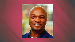 Business headshot of Marcus Anderson smiling in a blue blazer with a shaved head and goatee.
