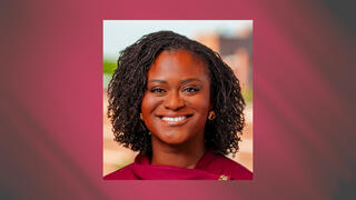 Professional portrait of Nana Asante-Smith smiling in a maroon top with natural curly hair and blurred city backdrop.
