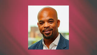 Corporate headshot of Stevie Dunk in a blue blazer and white shirt with a trimmed beard and earrings.