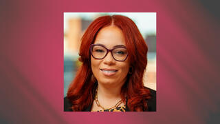 Professional portrait of Trish Hardy Wray with red hair and glasses wearing a black blazer and gold necklace.
