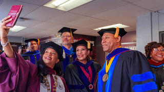 Chancellor Dixon and a group of faculty members in academic regalia gather together to take a selfie indoors.