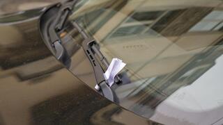 A folded paper ticket rests tucked under the windshield wiper of a dark car.