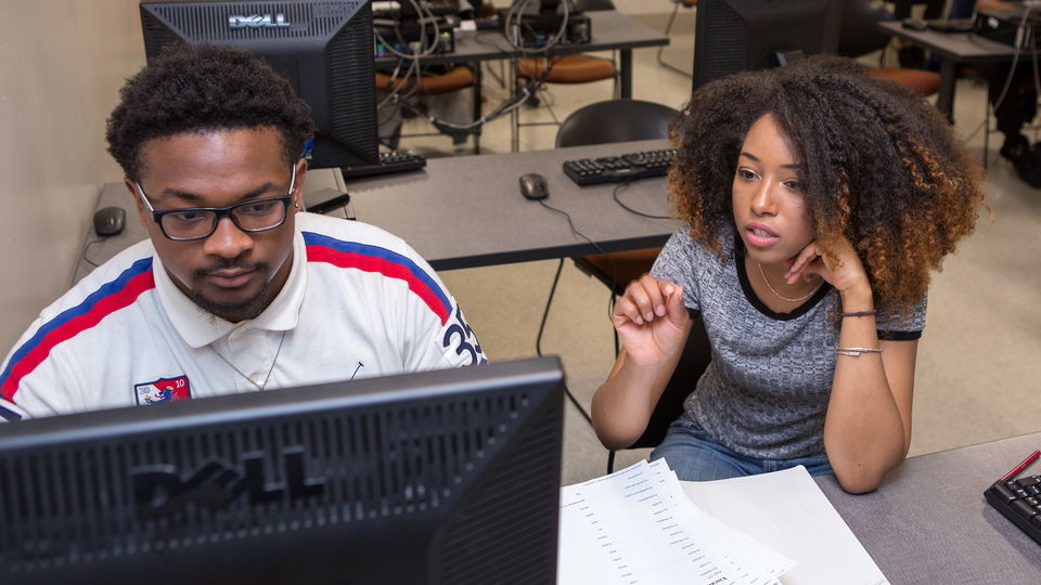 Tutor helping student at a computer.