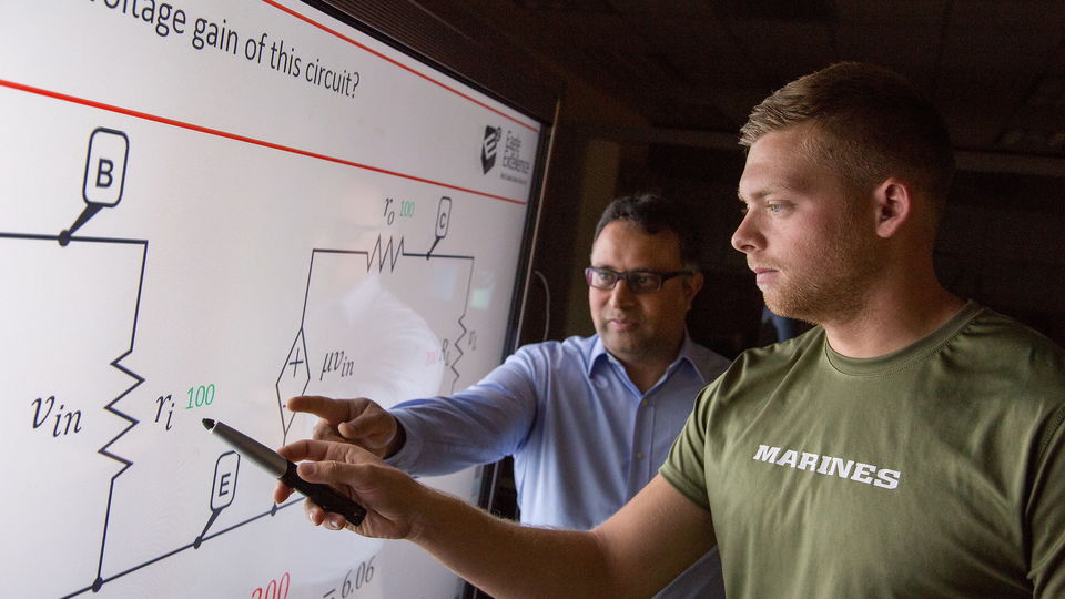 Physics teacher and student in classroom working on a smart board.