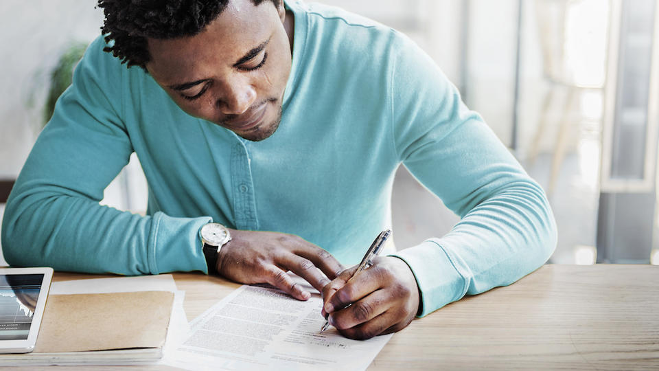 African American man in blue short writing at a table.