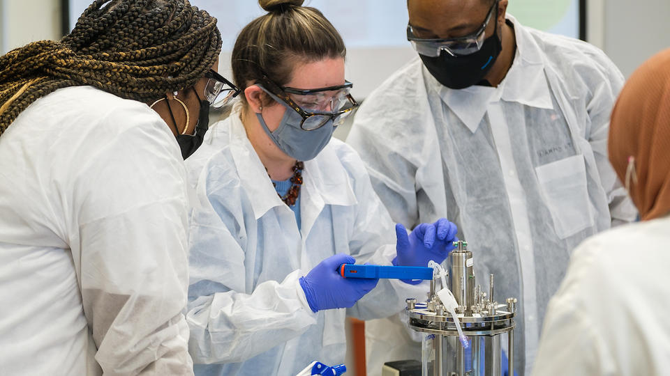 four people in white coats standing at a lab table