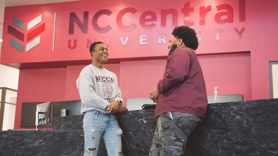 Two student speaking to each other in front of a reception desk