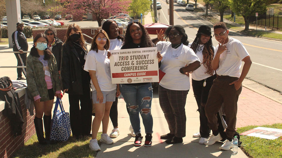 Students holding sign that says "TRIO Student Access & Success Conferences, Campus Guide"