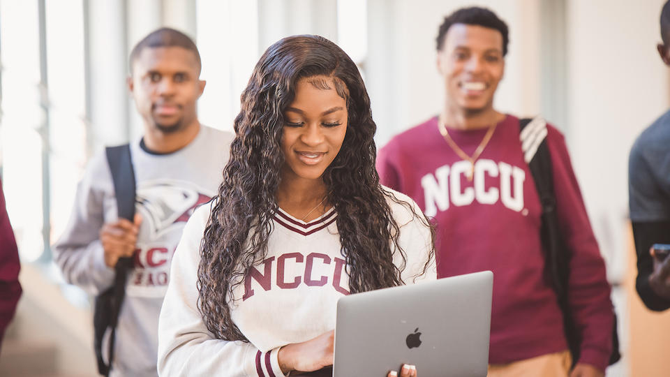 girl student looking at laptop with boy students in background