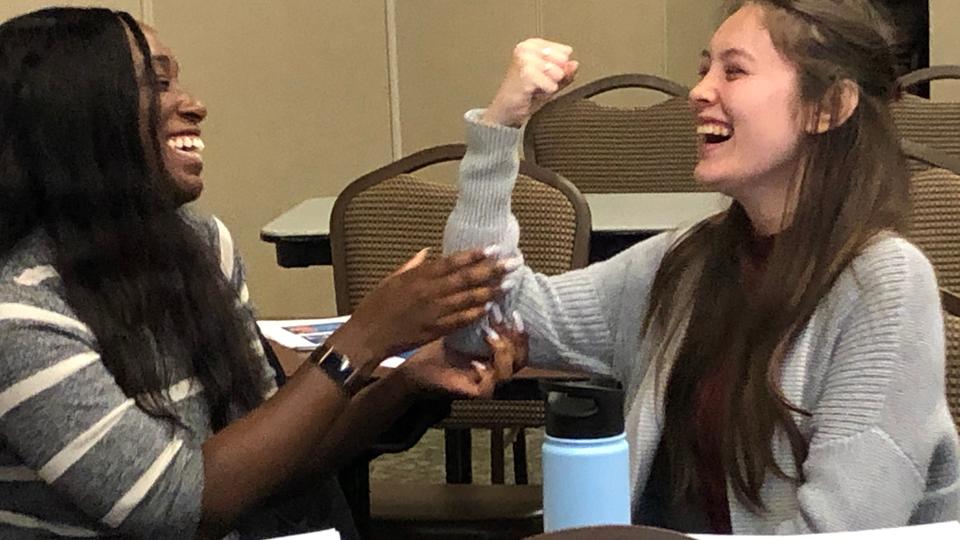 Two students laughing while one holds the other's elbow