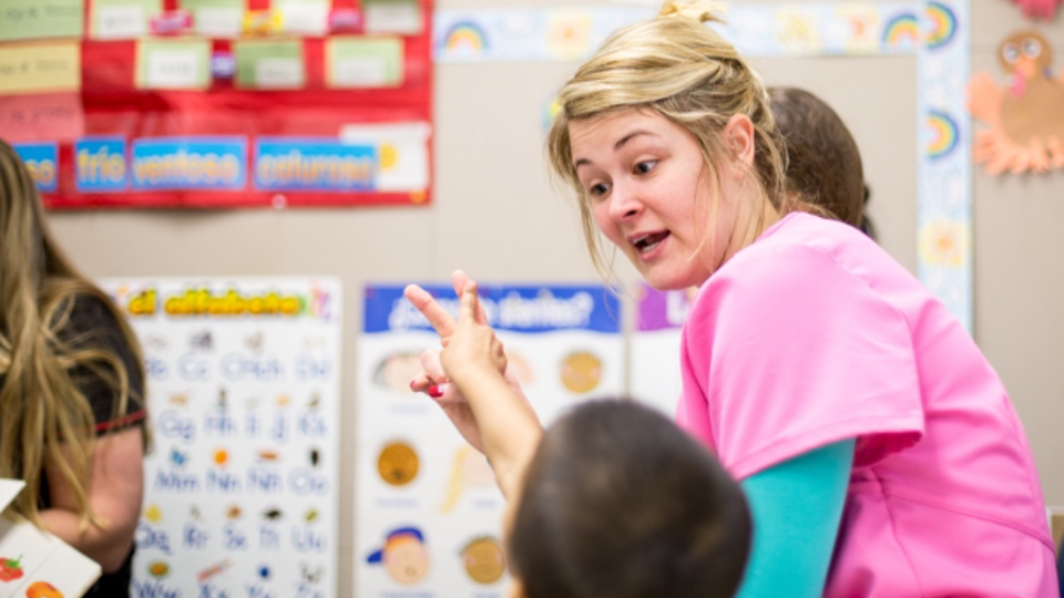 An closeup of an adult working with a group of children while pointing at posters