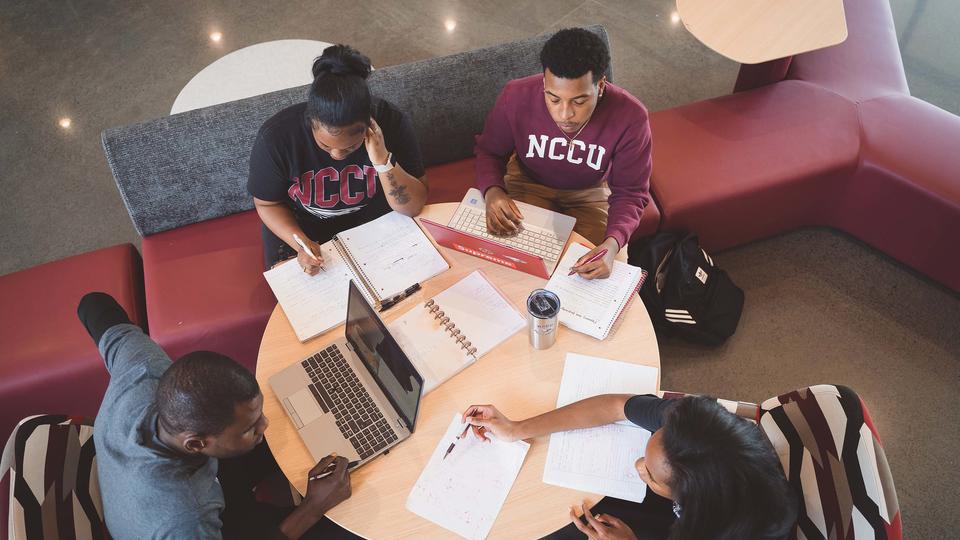 Four students sit at a small table studying together