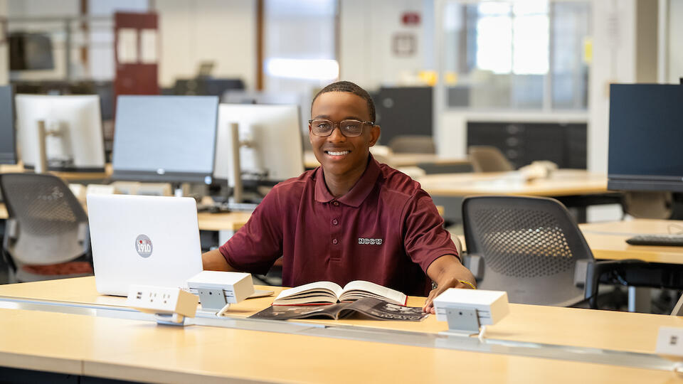 Eagle student in library with laptop and book
