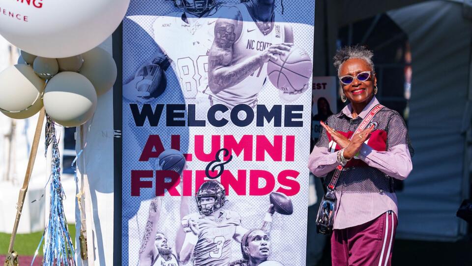 african american woman beside a retractable banner that has welcome alumni and friends