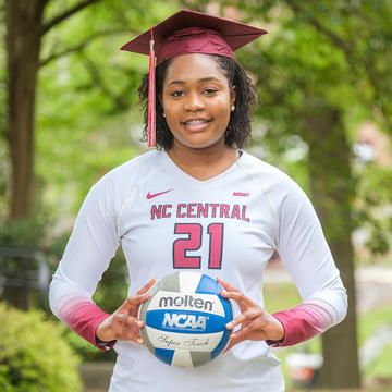 Volleyball player wearing graduation cap while holding volleyball.
