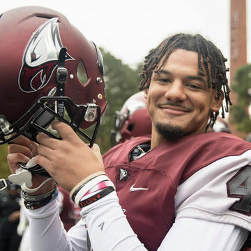 Student athlete holding up American football helmet