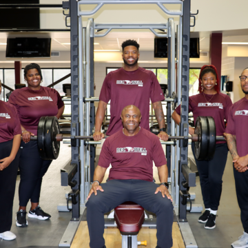 Members of the RecWell team standing and smiling around a bench press machine.