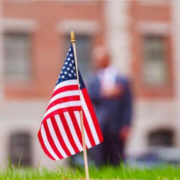 US flag in the foreground while someone is blurrily saluting
