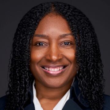 Professional headshot of Clastrola “Classy” Williams smiling against a dark background, wearing a dark blazer and white blouse with naturally curly hair.