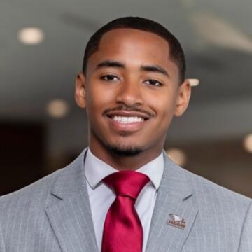 Professional headshot of Haneef A. Eiermann wearing a gray suit, white shirt, and red tie, smiling at the camera.