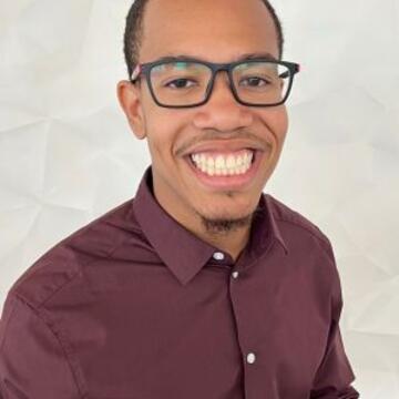Professional portrait of Will Watts smiling, wearing glasses and a maroon button-down shirt.