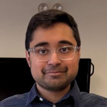 Professional headshot of Asaad Ahmed wearing glasses and a navy blue button-down shirt.