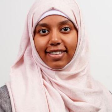 Professional headshot of Bana Alhassan wearing a light pink hijab and gray blazer.