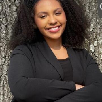 Professional portrait of Gabby McLeod smiling in a black blazer outdoors.
