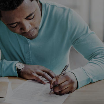 African American man in blue short writing at a table.