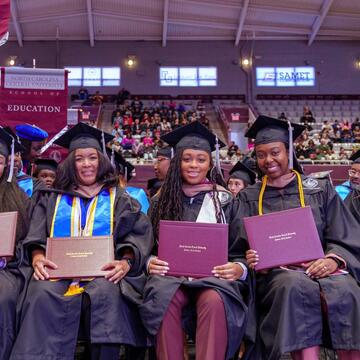 Graduates in caps and gowns holding diplomas, smiling at a ceremony.