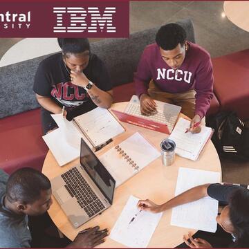 Group of Student sitting at table studying with notes and laptops.