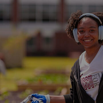 An NCCU student with headphones and gloves works in a garden
