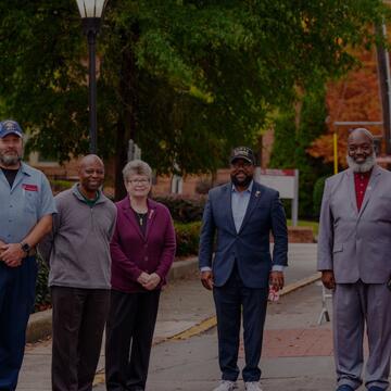 Group of six people, including veterans and university staff, stand outdoors on a campus walkway surrounded by fall foliage during a Veterans Day event at North Carolina Central University.