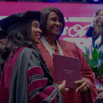 Chancellor Dixon smiles as she presents a diploma folder to a graduate at a North Carolina Central University commencement ceremony.