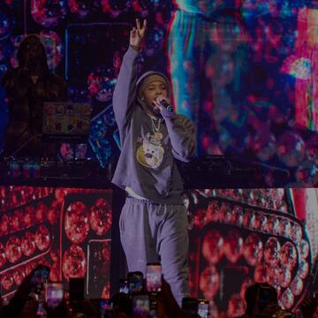 Rapper G Herbo holds up a peace sign while performing on stage in front of a crowd holding up smartphones.