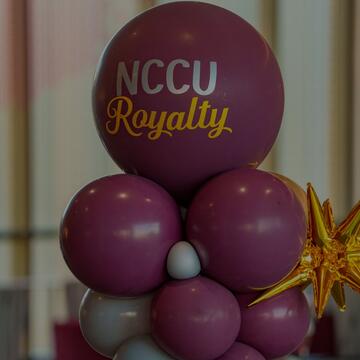 A balloon centerpiece feature maroon and white balloons with a large top balloon that reads "NCCU Royalty" in white and yellow text alongside a gold starfoil balloon accent.