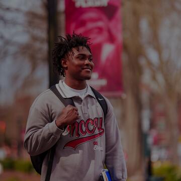 Student smiling and carrying a backpack and notebooks