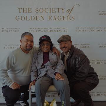 Three people pose in front of a backdrop that says "The Society of Golden Eagles"