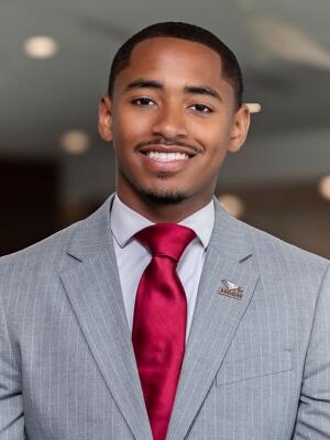Professional headshot of Haneef A. Eiermann wearing a gray suit, white shirt, and red tie, smiling at the camera.